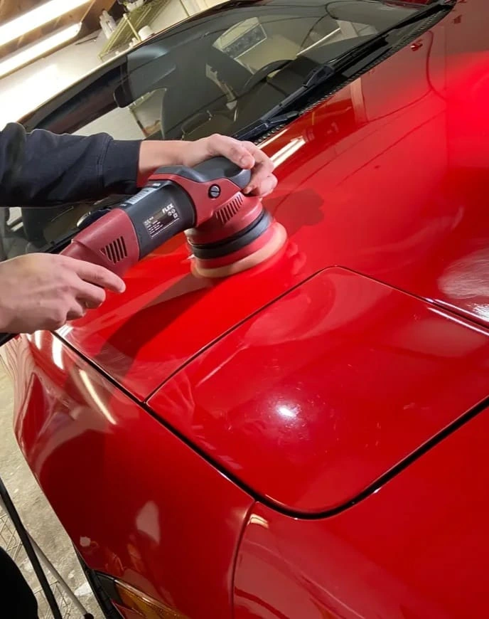 Technician using a rotary polisher on a red car hood to perform professional paint correction.