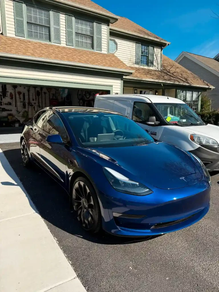 Blue Tesla freshly detailed on a St. Charles residential driveway by Pure Auto-Care mobile detailing service van visible in background